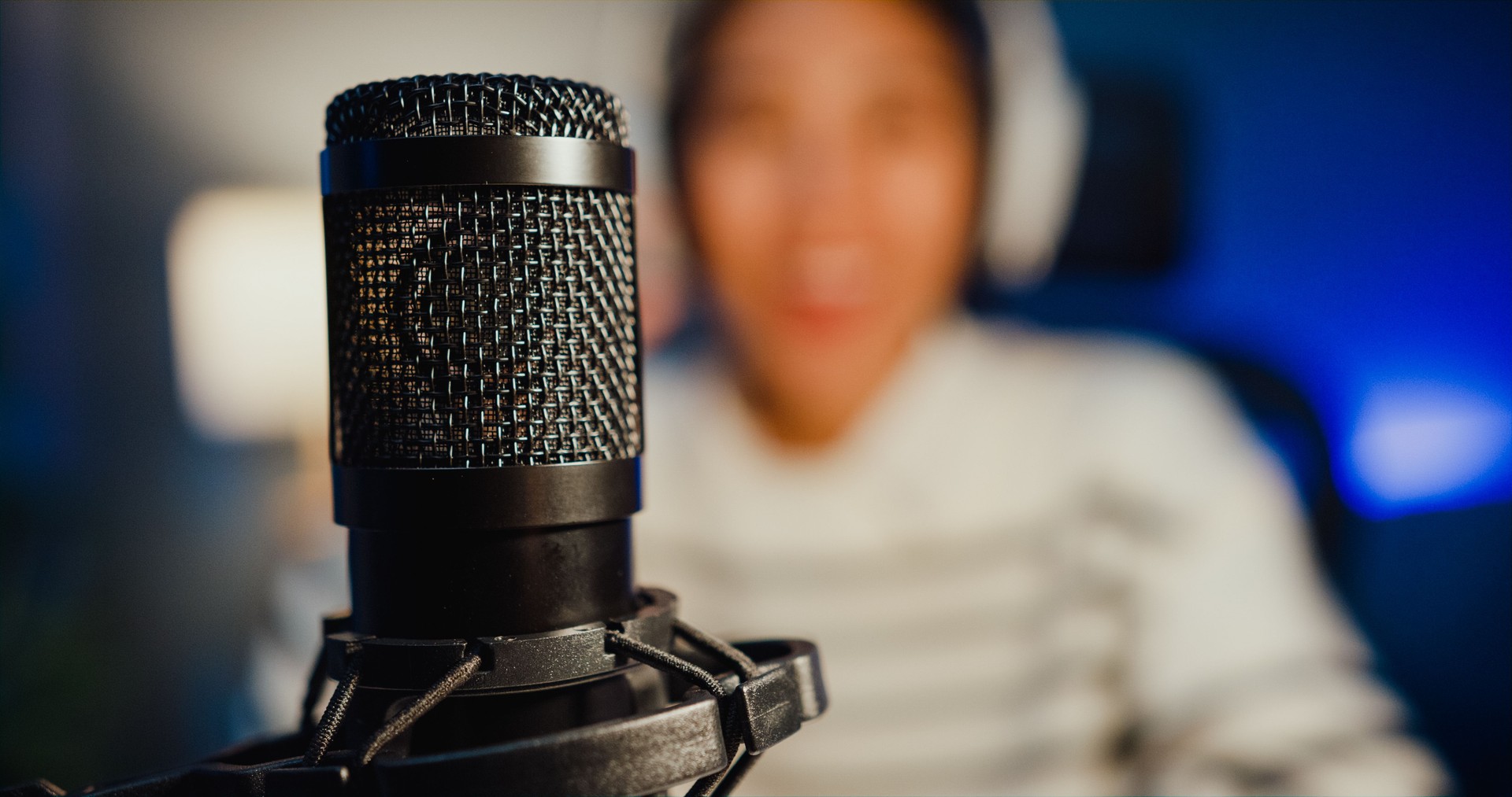 Happy asia lady blogger music influencer record a podcast on computer with headphones and microphone talk with audience in living room home studio at night.