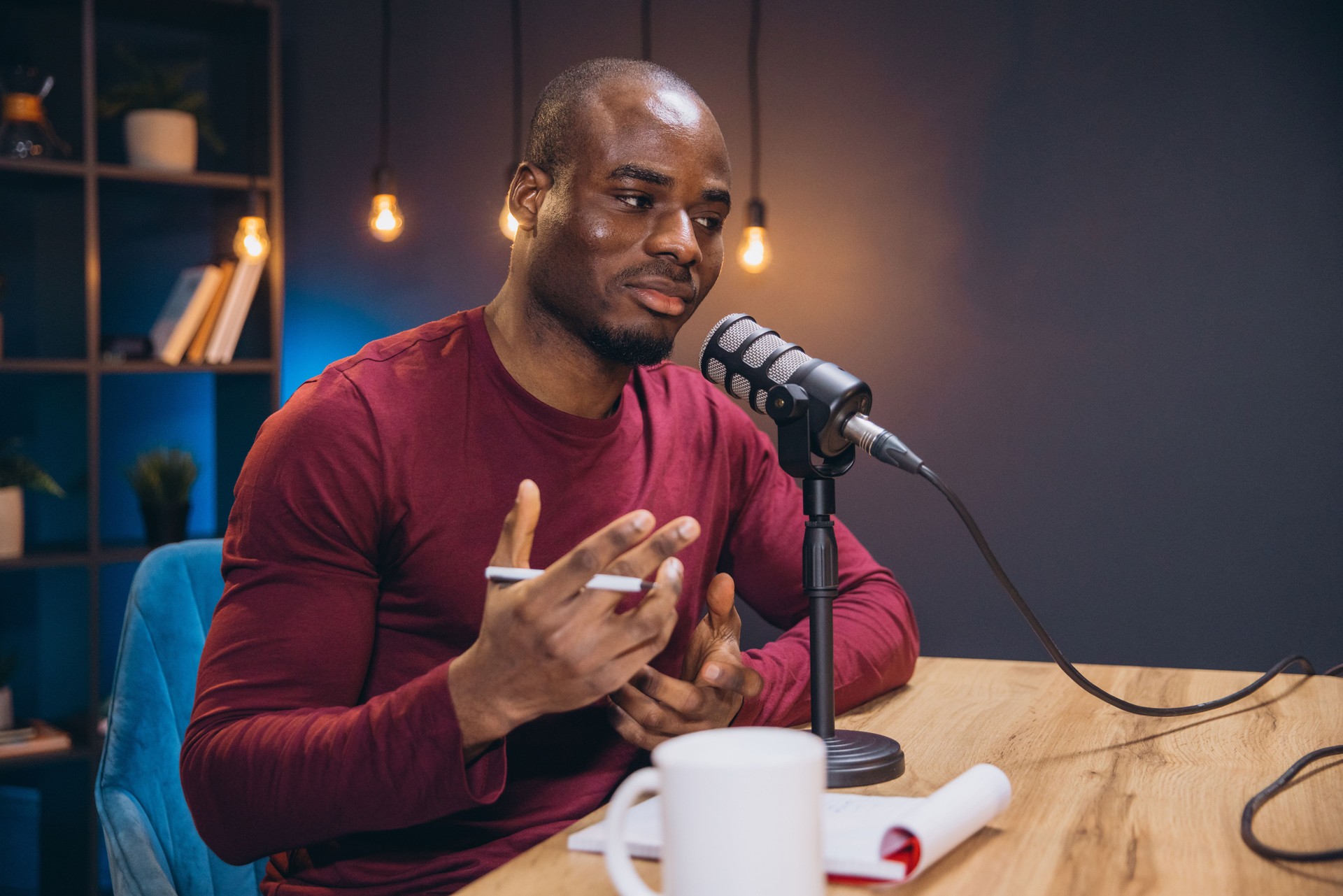Young African American man recording a podcast in a professional studio, speaking into a microphone and gesturing with his hands